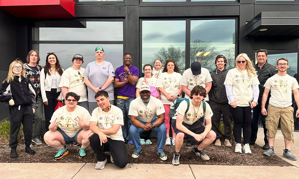 Group of people wearing matching T-shirts posing in front of a modern building with large glass windows.