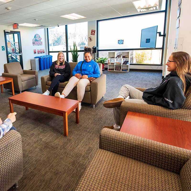 three female students sitting in a common area in perry hall, talking and smiling